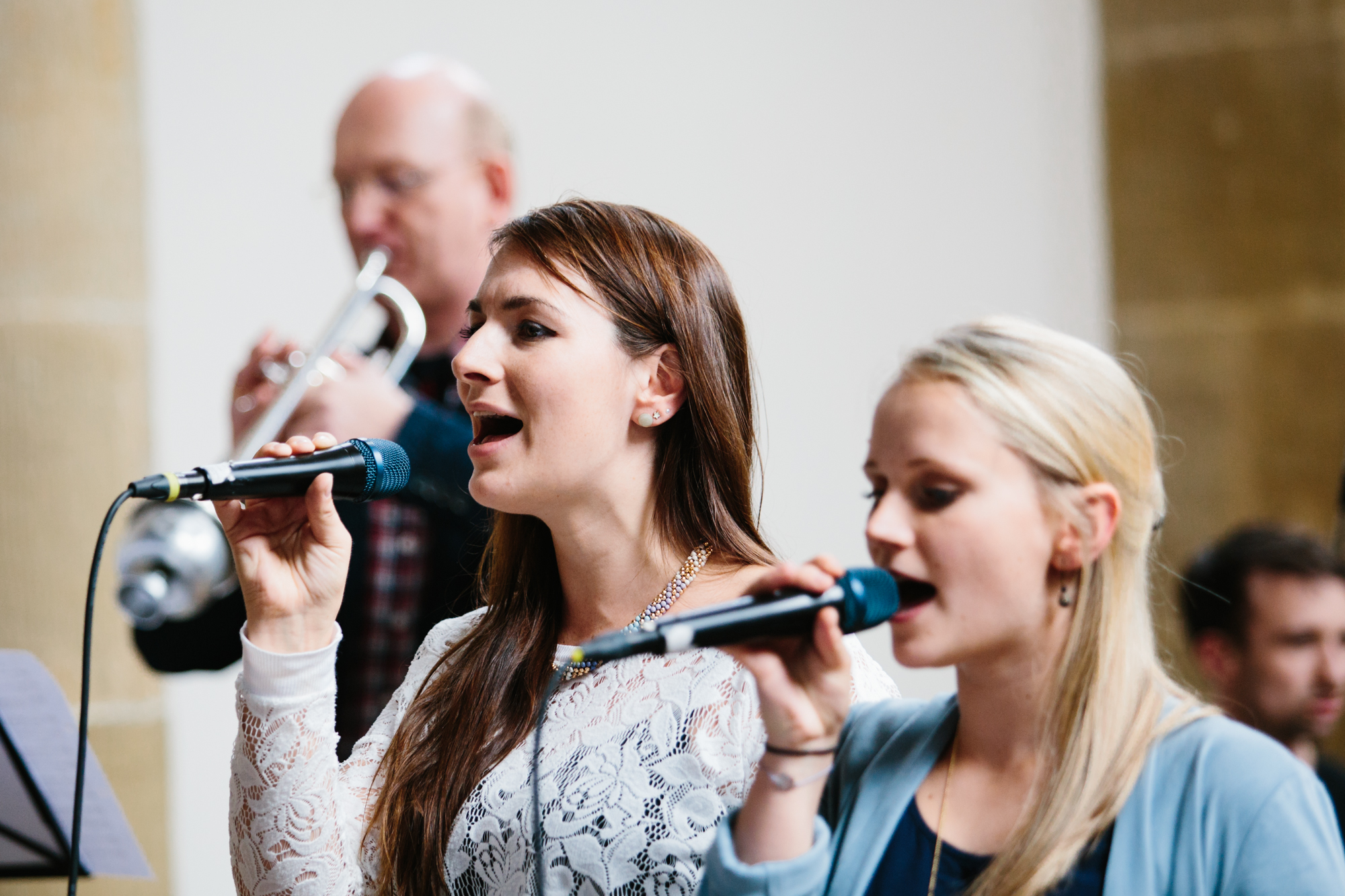 Mitglieder der Werkstatt Neues Geistliches Lied NGL singen mit Mikrofon; im Hintergrund spielt Tobias Lübbers Trompete.